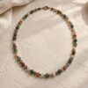 Gemstone necklace with green, smoky, cream, and muted rust beads on pale plaster