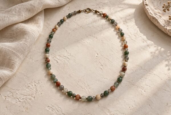 Gemstone necklace with green, smoky, cream, and muted rust beads on pale plaster